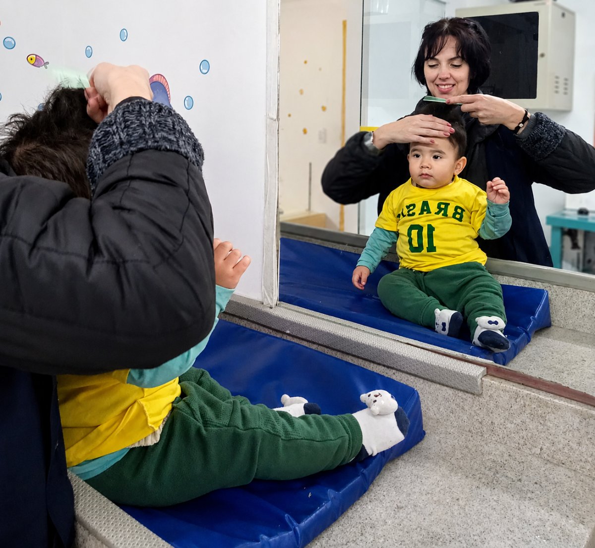 Professora penteando bebê em frente ao espelho