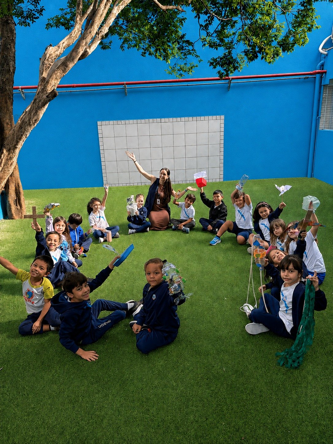 Alunos e professora reunidos no jardim com trabalhos manuais em atividade ao ar livre