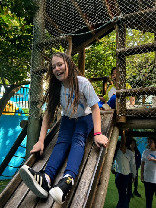 Aluna sorrindo ao descer no escorregador do parque