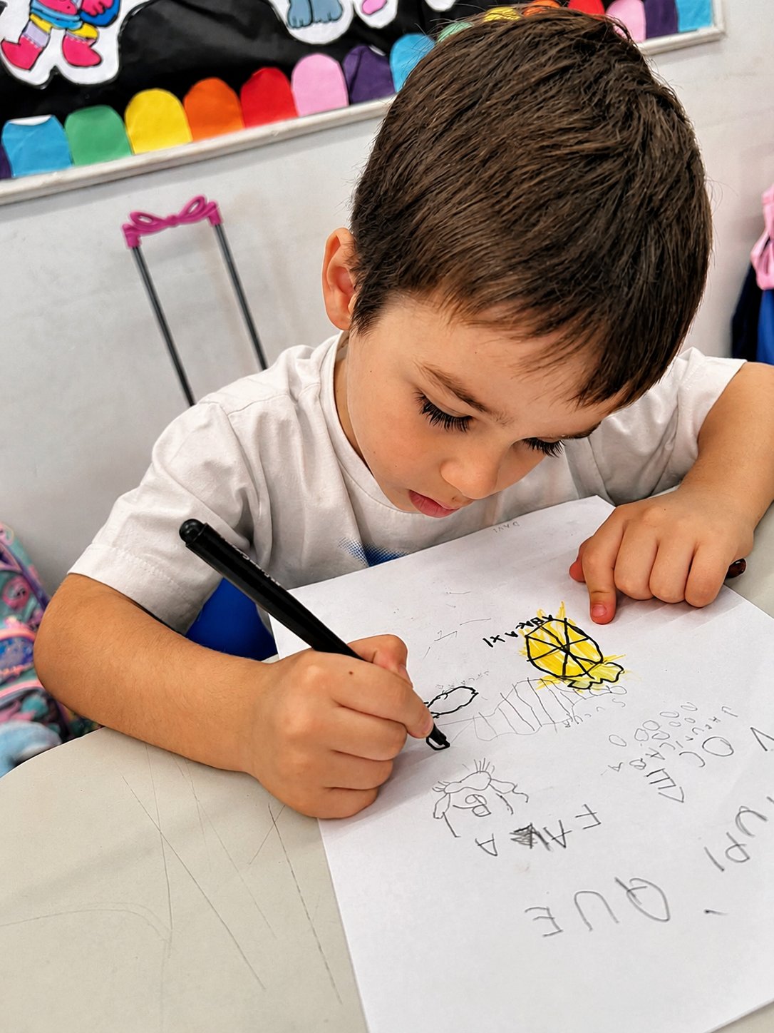 Menino escrevendo e desenhando na atividade de alfabetização